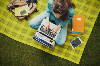 Woman sitting on a blanket outside working on a laptop.