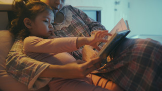 A young girl reads a book with her mother. 