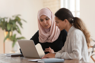 two middle eastern girls sitting around laptop working